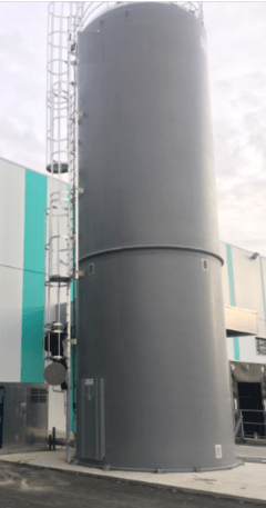 Industrial rigid silo in anthracite grey equipped with a ladder and steel guardrail, installed in front of a white and turquoise panel façade.